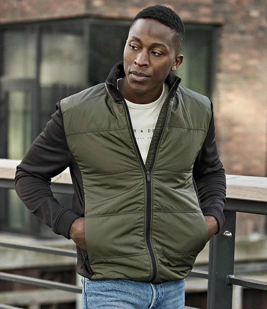 Man wearingTee Jays blank stretch padded jacket with black sleeves and deep green body